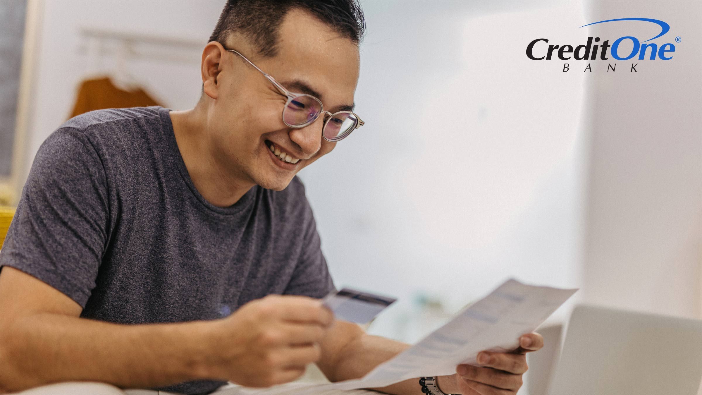 A man holds a credit card in one hand as he reviews a document he’s holding in the other. He is smiling, perhaps because this is the first step he’s taking toward rebuilding his  credit with credit cards.