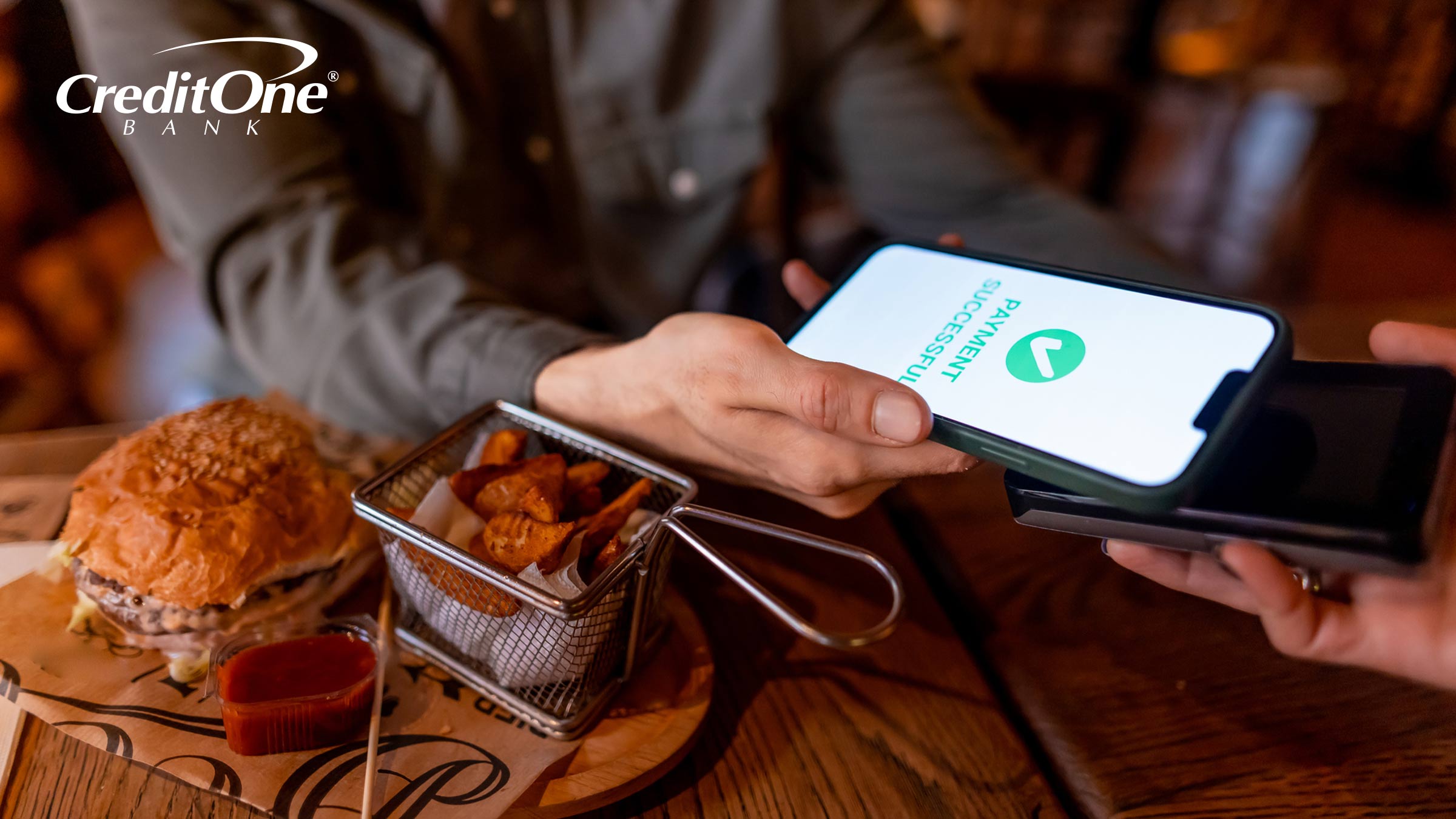 A man pays for his restaurant meal by tapping his phone to a handheld card terminal. Mobile wallet payments like this use credit card tokenization for security.