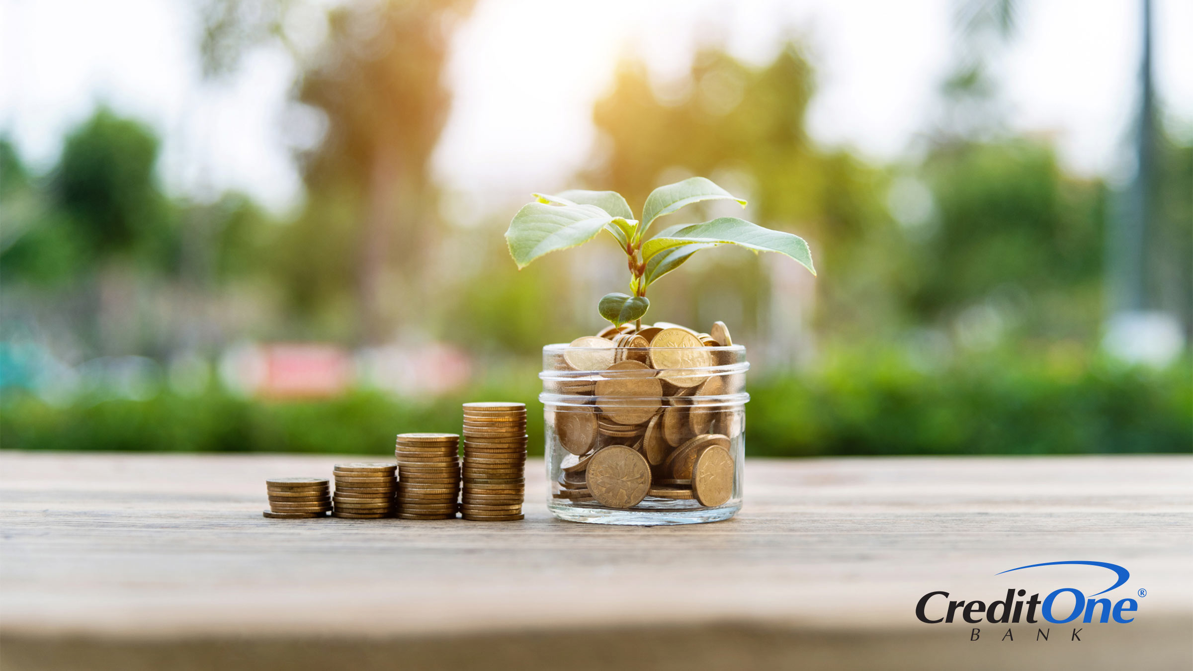 Four increasingly tall stacks of coins are set beside a jar, which is also filled with coins and has a small plant sprouting from it. This represents the act of investing and growing wealth.
